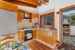 Une cuisine avec des meubles en bois, une cuisinière, un four à micro-ondes et une vue sur les montagnes par une fenêtre.