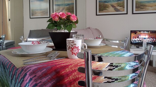 A dining area with a table set for four, a potted plant with pink flowers, and a television displaying an audience. - Suite with moons of the Amazon River, by Reforma 222 (Ciudad de México)