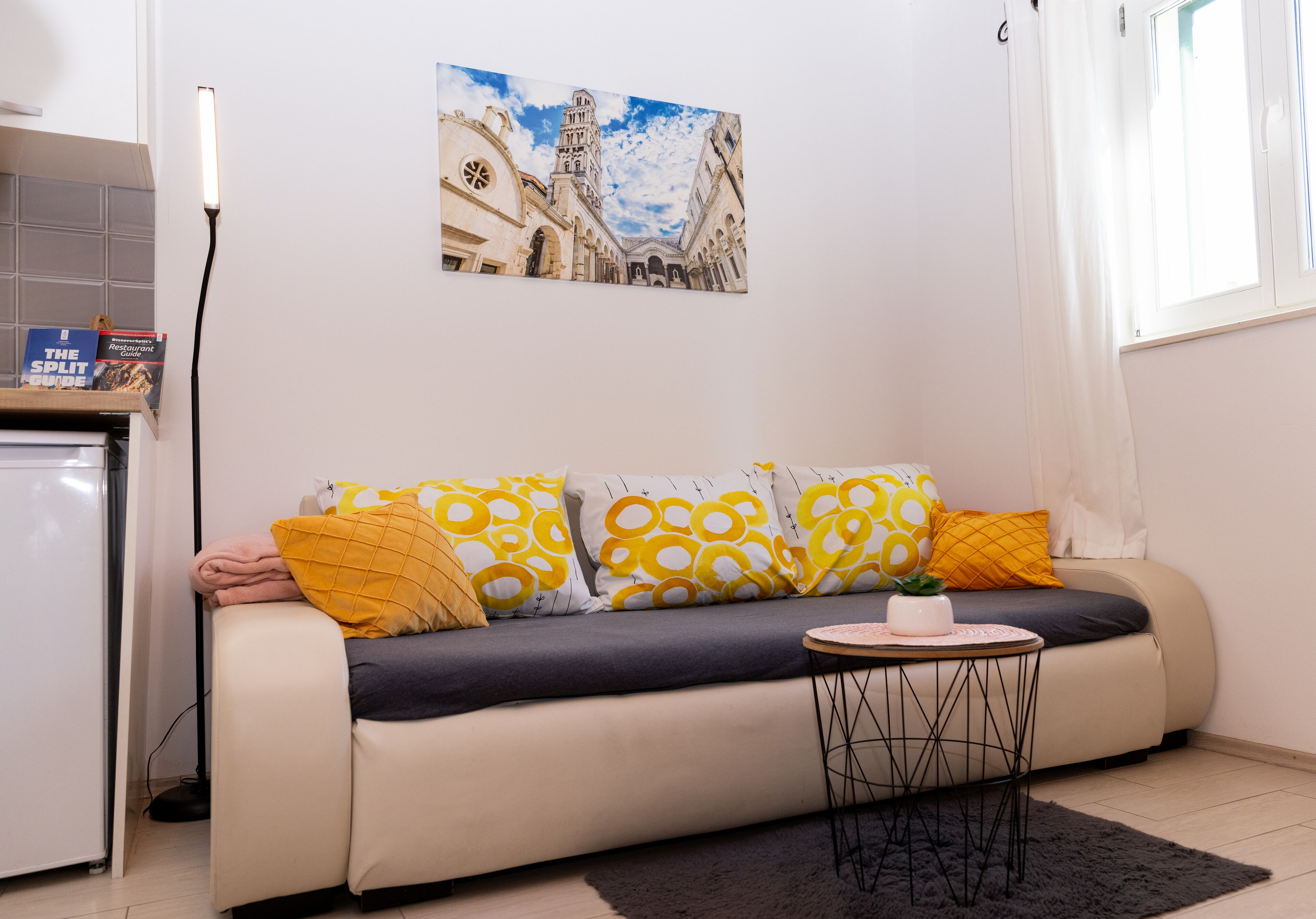 Una sala de estar con un sofá, una mesita con una planta y un cuadro de un edificio en la pared.