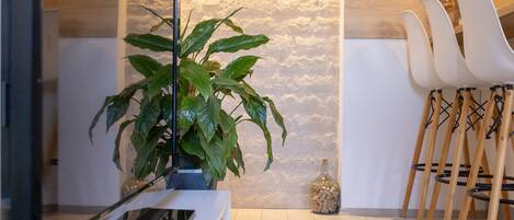 Een moderne woonkamer met een stenen accentmuur, een potplant en een eethoek met witte stoelen.