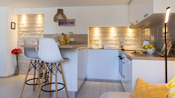 A modern kitchen with a central island, bar stools, a vase with flowers, and a 'TEA TIME' sign. - Rooms and apartments Paese (Split)