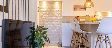 A modern kitchen with white chairs, a wooden dining table, and a hanging pendant light.