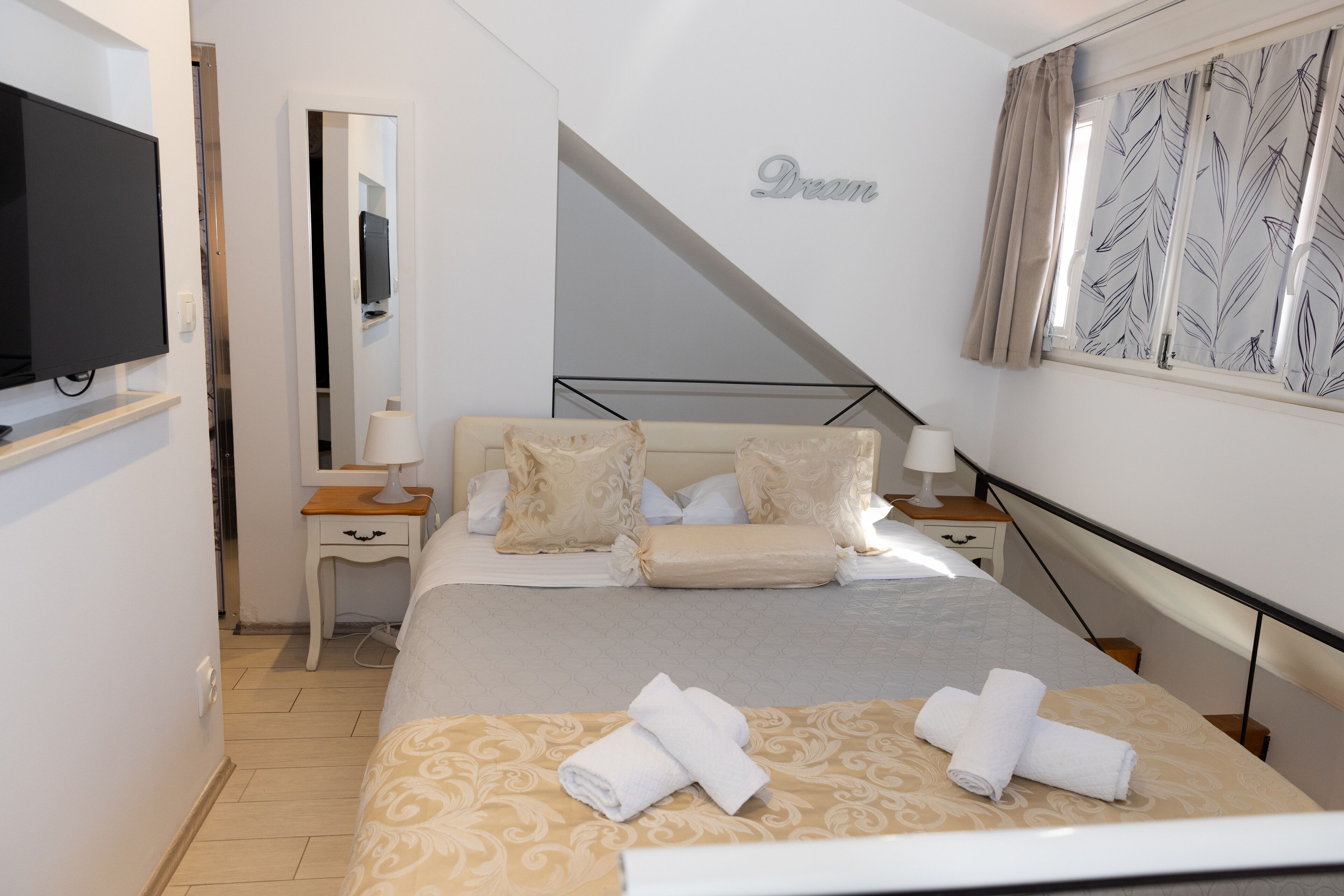 A hotel room with a bed, two bedside tables, a TV, a mirror, and a window with curtains.