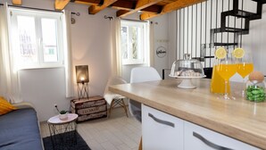 A cozy room with a wooden ceiling, a bed with a blue bedspread, a small round table with a plant, a white chair, and a kitchen area with a wooden countertop and a fruit bowl. - Rooms and apartments Paese (Split)