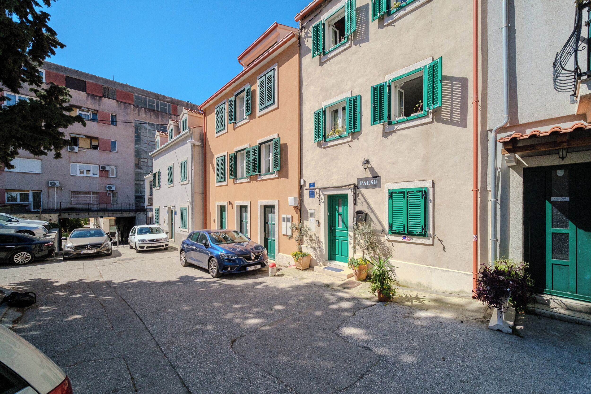 A row of buildings with green shutters, parked cars, and a clear blue sky.