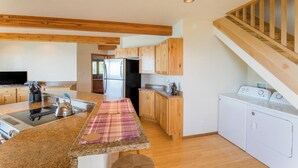 Una cocina moderna con encimeras de granito, armarios de madera, refrigerador de acero inoxidable, horno empotrado y lavadora.