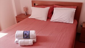Una cama bien hecha con un edredón rojo, almohadas blancas y una toalla doblada al lado.