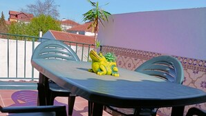 Un patio con una mesa y sillas, una estatua decorativa de rana y un muro de azulejos.