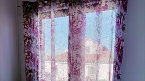 Una habitación con una cama, cortinas florales y una ventana con vistas a edificios.