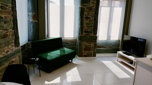A room with a stone wall, a green sofa, a TV, and a dining table with cutlery.