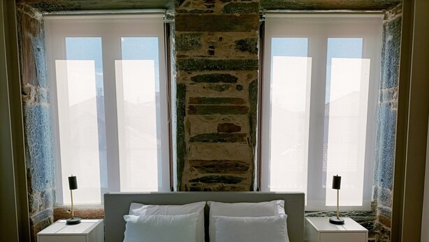 A bedroom with a bed, two bedside tables, a stone wall, and large windows.