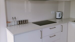 A kitchen with white cabinets, a black countertop, and a kettle.