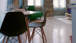 A dining area with a stone wall, a green cushioned bench, a table with chairs, and a television on a stand.