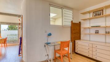 A room with a glass desk, an orange chair, a wooden cabinet, and a window with blinds.