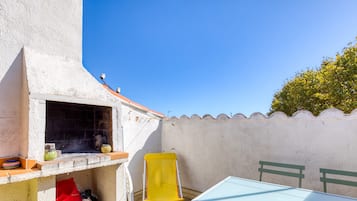 Terassi, jossa on pöytä ja tuoleja, pieni grilli ja seinä, jossa on ikkuna.