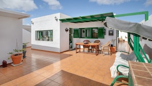 Un patio con una mesa, sillas, un toldo verde y plantas en macetas.