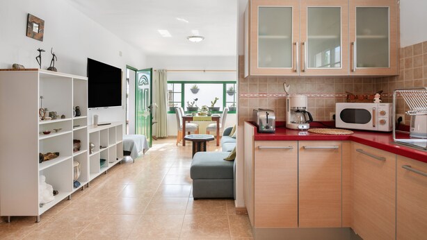 Una cocina moderna con armarios empotrados, un comedor con mesa y sillas, y un televisor montado en la pared.