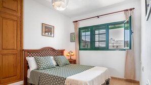 Un dormitorio con cama, armario de madera, ventana con cortinas y una lámpara de pared.
