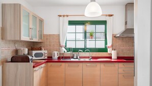 Una cocina con armarios de madera, microondas, lavamanos y ventana con marco verde.