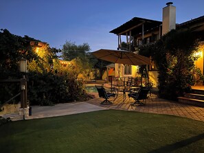 Une terrasse avec une table et des chaises, une piscine et un espace couvert d’où l’on a vue sur la maison.