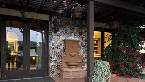 Una entrada de edificio con un muro de azulejos, una fuente de piedra y un patio cubierto.