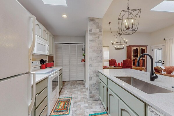 A kitchen with white cabinets, a large island with a sink, and a decorative chandelier.