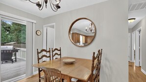 Un comedor con una mesa y sillas de madera, un espejo redondo en la pared y vistas al exterior.