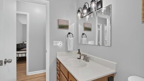 Un baño con lavamanos blanco, tocador de madera y espejo con lámpara.