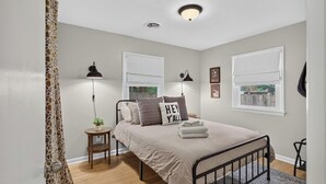 A bedroom with a bed, bedside lamps, a small table, and a window with a view.