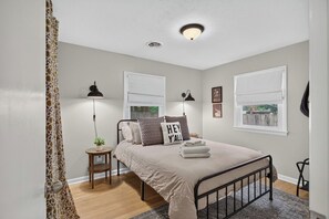 A bedroom with a bed, bedside lamps, a small table, and a window with a view.