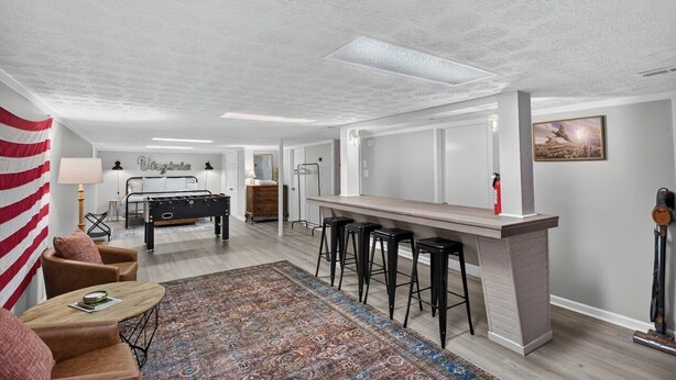 A spacious living room with a pool table, bar stools, and a large rug.