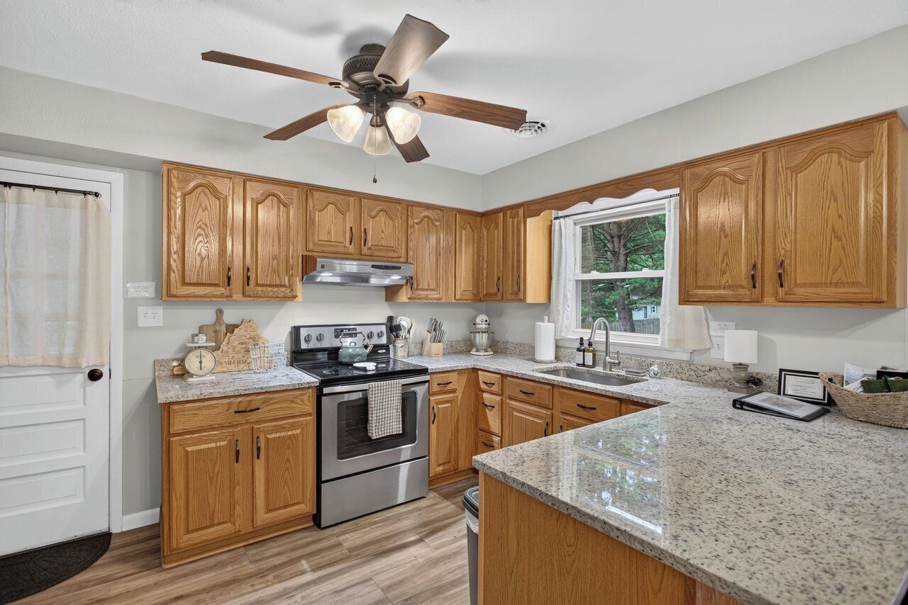 A kitchen with wooden cabinets, a stainless steel oven, granite countertops, and a ceiling fan.