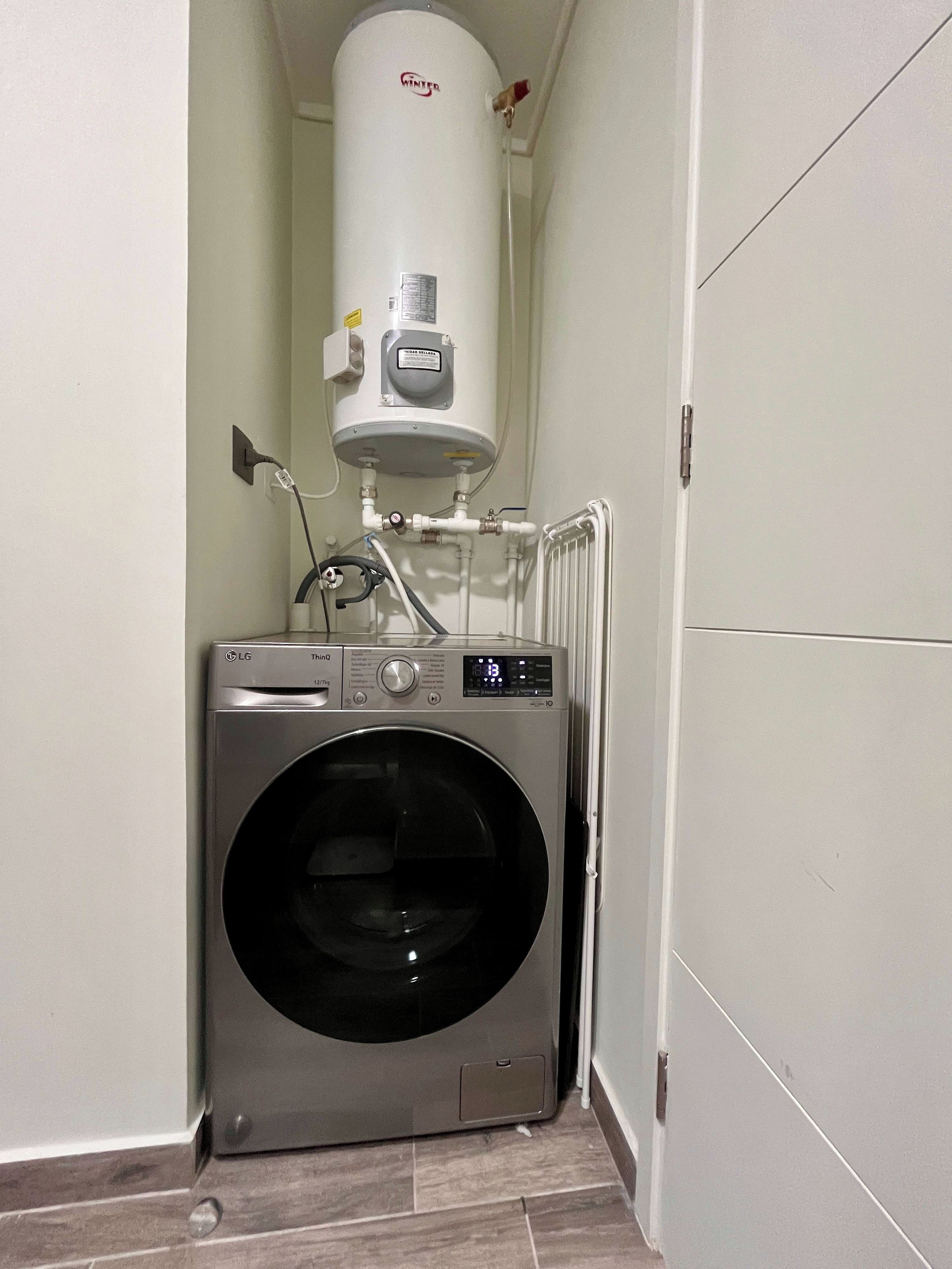 Een kleine wasruimte met een voorlader wasmachine en een boiler.