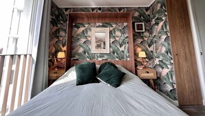 Una camera da letto con un letto, due comodini, uno specchio e una parete con un motivo a foglia tropicale.