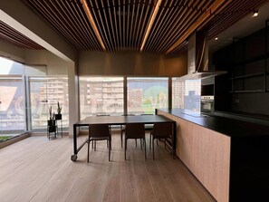 A modern kitchen with a wooden ceiling, large windows, and a dining area with chairs.