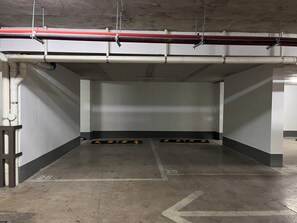 An empty parking garage with concrete walls, a ceiling with exposed pipes, and directional arrows on the floor.