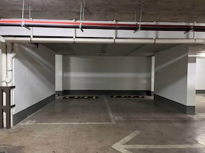 An empty parking garage with concrete walls, a ceiling with exposed pipes, and directional arrows on the floor.