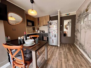 A compact kitchen with a dining table, chairs, and a refrigerator adorned with stickers. - Artistic Ñuñoa Apt - Projector, Parking & Metro (Ñuñoa)