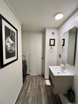 A bathroom with a framed artwork, a toilet, a sink, and a mirror. - Artistic Ñuñoa Apt - Projector, Parking & Metro (Ñuñoa)