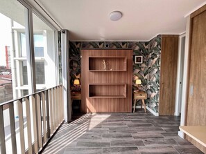 Un pasillo con una estantería de madera, una mesita con una lámpara y vistas al exterior a través de un ventanal.
