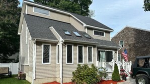 Ein zweistöckiges Haus mit Veranda, einer kleinen Terrasse und einem Garten mit roter Rindenmulch.