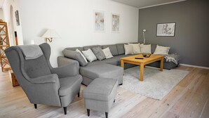 Ein modernes Wohnzimmer mit einem grauen Ecksofa, einem grauen Sessel, einem Holztisch und einem weißen Teppich.