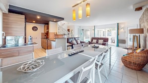 A modern kitchen with a dining area, a living room with a sofa and chairs, and a large window providing natural light. - Lovely home in Moëlan-sur-Mer with sauna (Moëlan-sur-Mer)