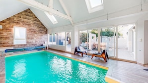 An indoor swimming pool with a wooden wall, a seating area with chairs, and a glass door leading to an outdoor patio. - Lovely home in Moëlan-sur-Mer with sauna (Moëlan-sur-Mer)