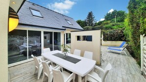 A modern patio with a white table and chairs, a glass door leading to an outdoor seating area, and a small enclosed space with a window. - Lovely home in Moëlan-sur-Mer with sauna (Moëlan-sur-Mer)