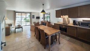 Une cuisine spacieuse avec des meubles en bois, une table à manger entourée de chaises en osier et une grande fenêtre qui laisse entrer la lumière naturelle.