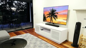 Una sala de estar moderna con una televisión de pantalla plana sobre un mueble blanco, una alfombra estampada y una lámpara de pie negra.