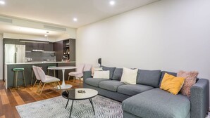 Una sala de estar moderna con un sofá gris, una mesita redonda y una cocina al fondo.