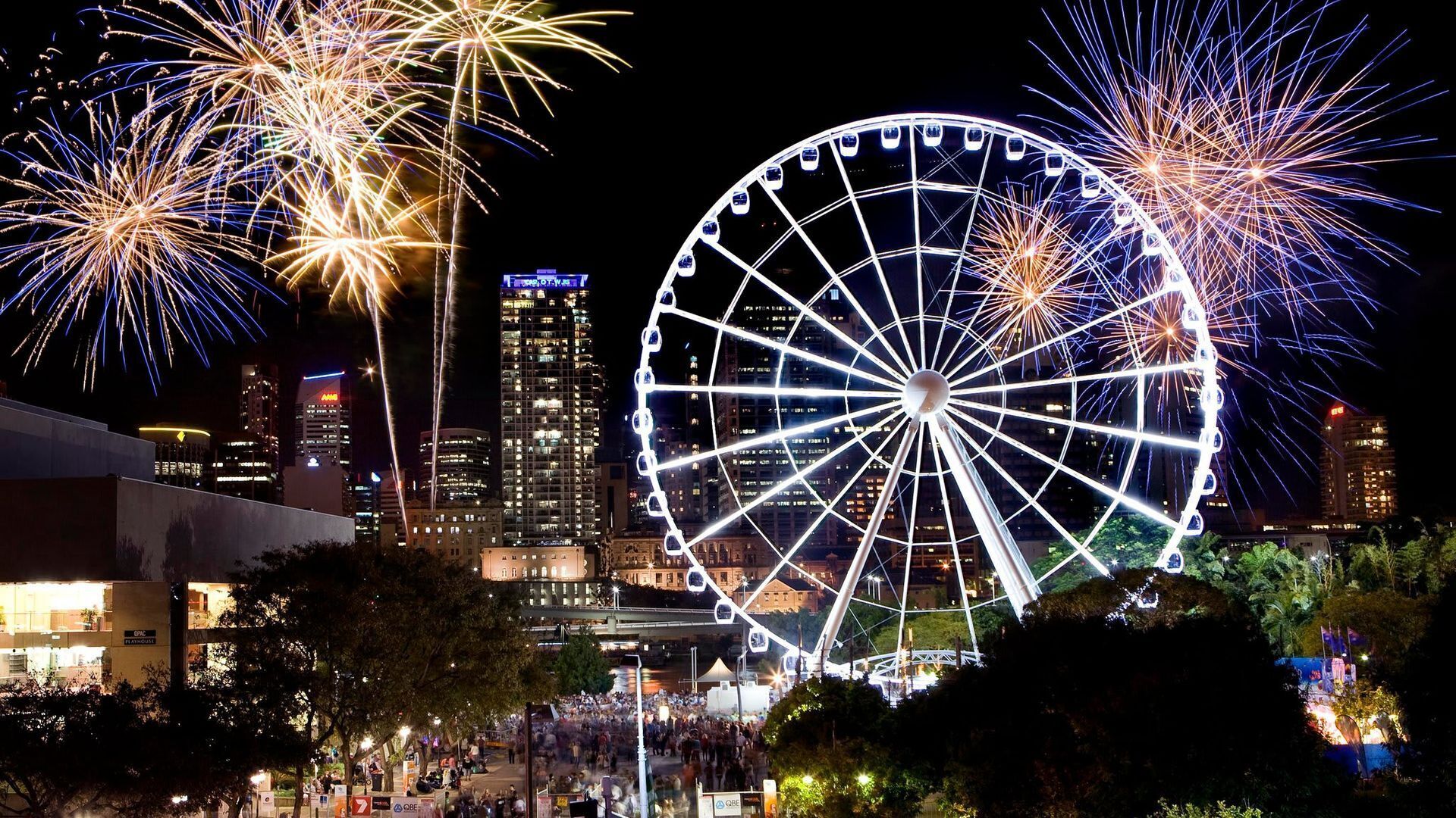 A Ferris wheel and fireworks in a cityscape at night.