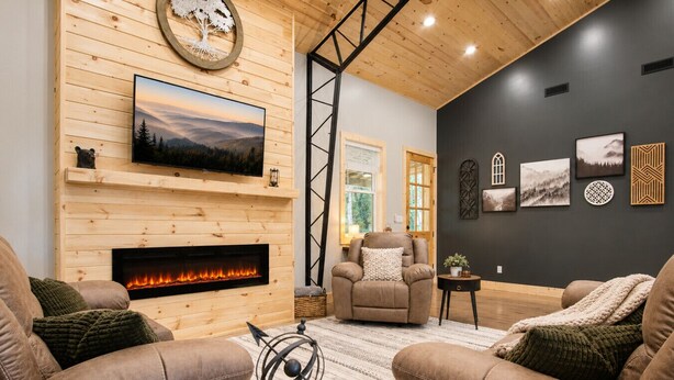 Un salon chaleureux avec une cheminée, des canapés en cuir, une table basse et un téléviseur fixé à un mur en bois.